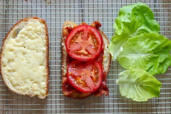 A slice of bread with cheese and a slice of bread with bacon and tomato and lettuce