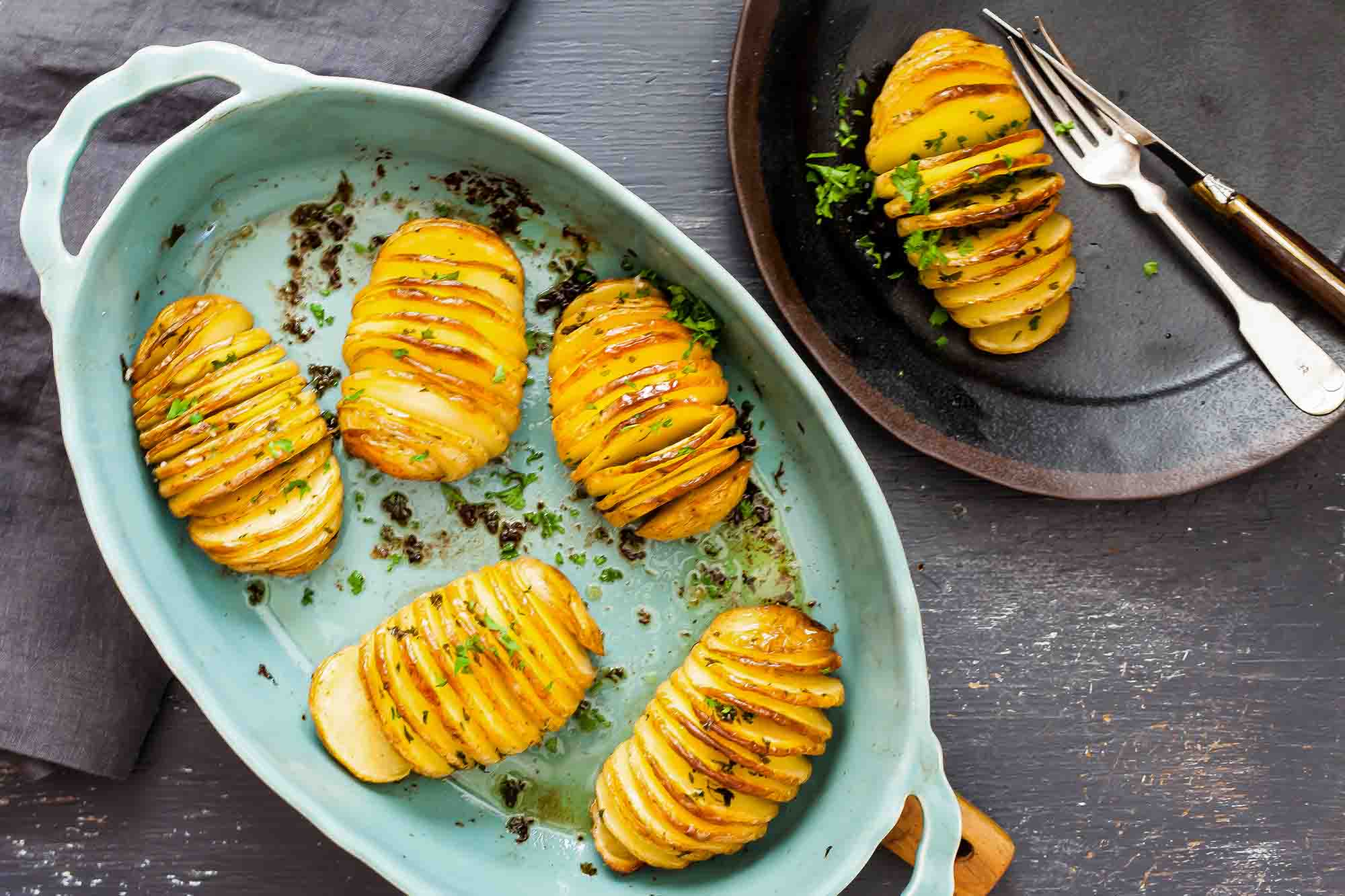 Hasselback potato recipe potatoes cut accordion style in a baking dish with herbs, butter, and olive oil.