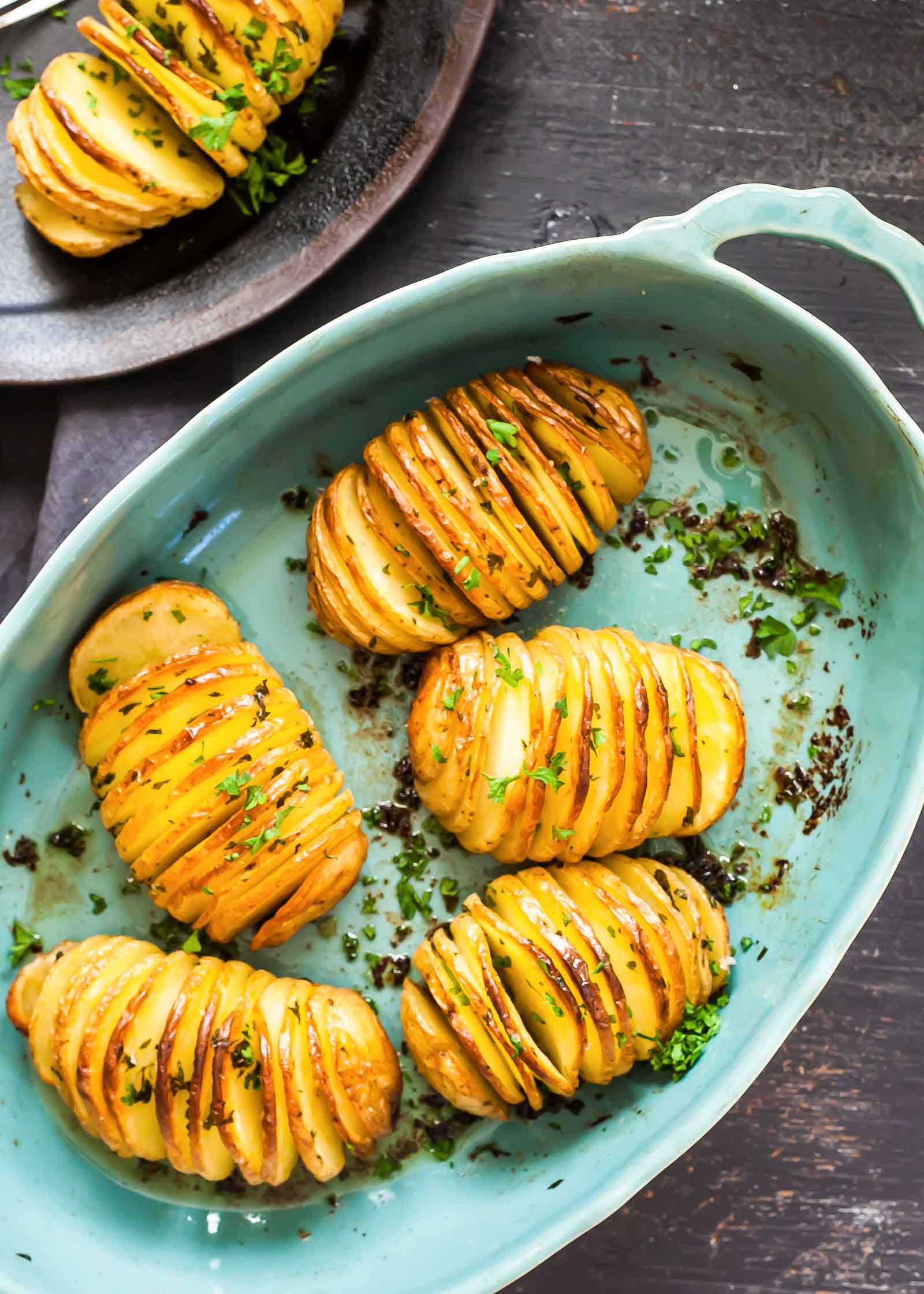 Hasselback Baked Potatoes Baked potatoes in a blue dish with herbs and olive oil.