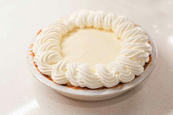 Whole banana cream pie with whipped cream swirls on top set against a white background.