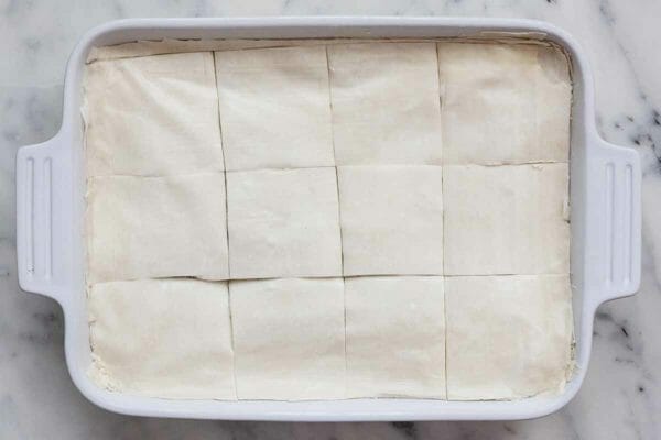 Phyllo cut into squares lining the top of of a casserole dish filled with spinach and cheese for spanakopita.