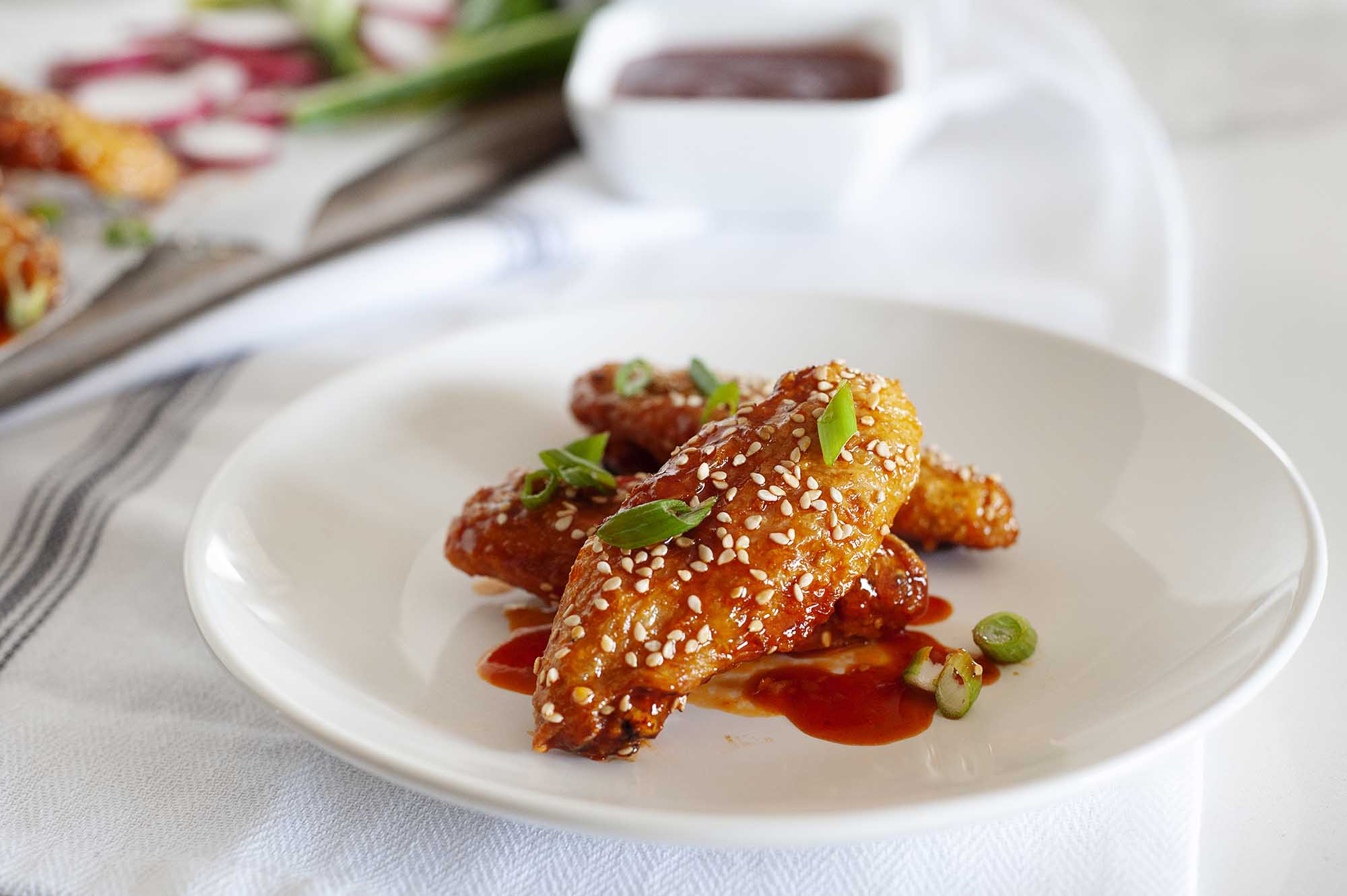 Air Fryer Chicken Wings with Gochujang Sauce and Sesame Mayo dip on a white plate sprinkled with scallions and sesame seeds.