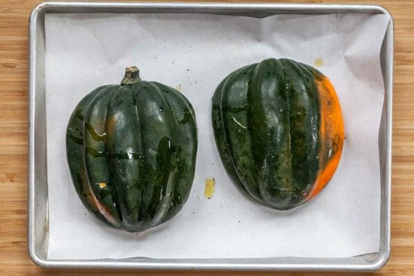 Acorn Squash sliced in half on a sheet of parchment. The sliced half is facing down.