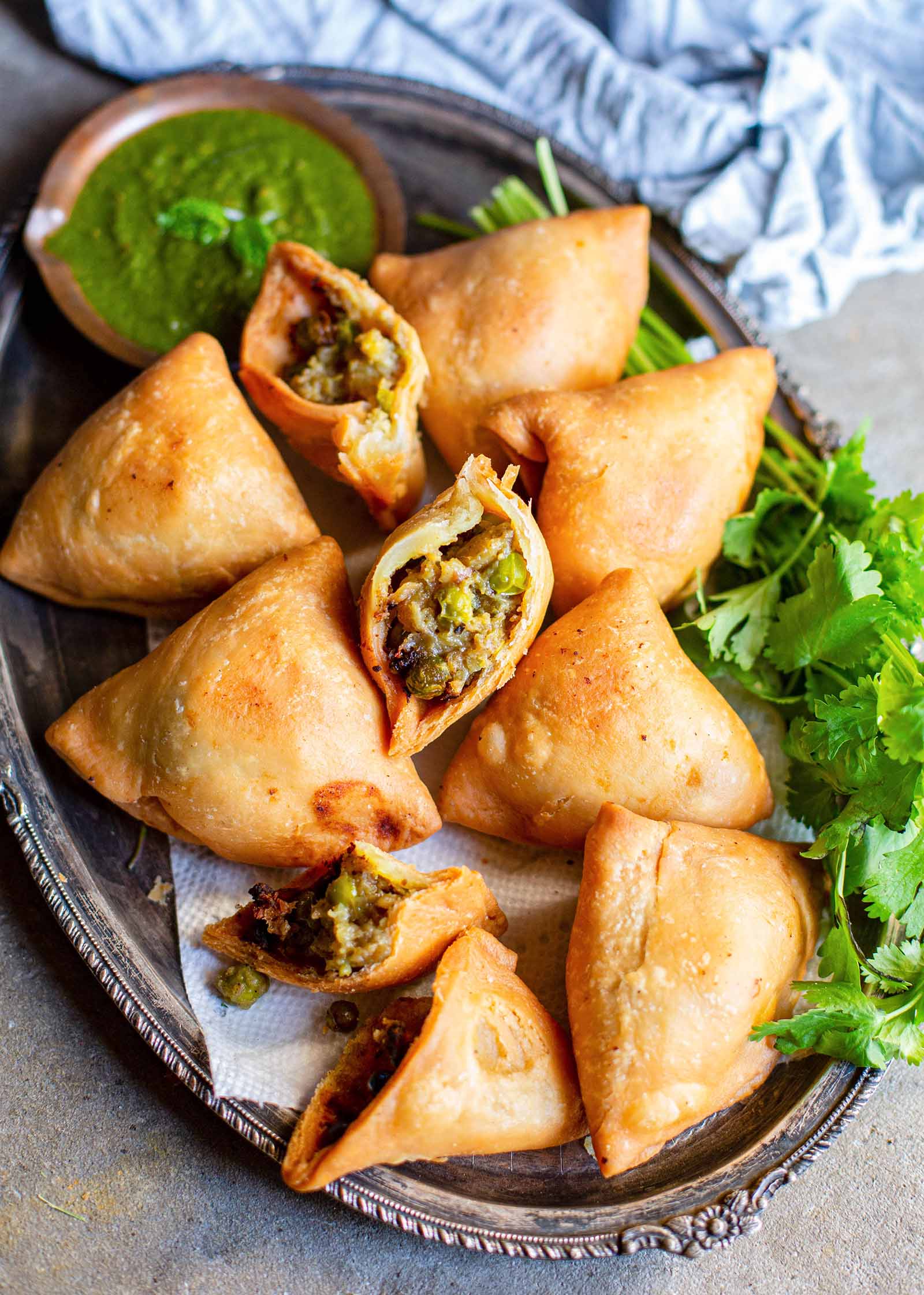 Golden Vegetarian Samosas on a bed of herbs with one samosa broken open to show the potato and pea filling.
