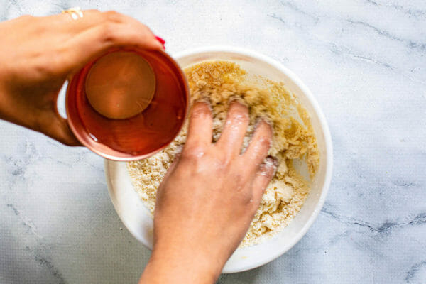 Woman's hand mixing Ingredients to make dough -- flour, slat and butter or ghee in three small bowls on a marble counter and adding water from a copper cup into the bowl.
