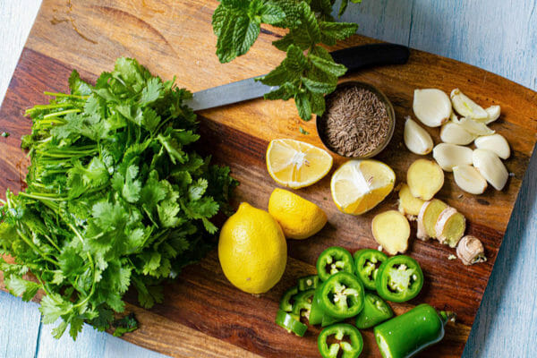 Cilantro, mint, lemons, cumin, ginger, garlic and jalapenos chopped on a wooden cutting board.
