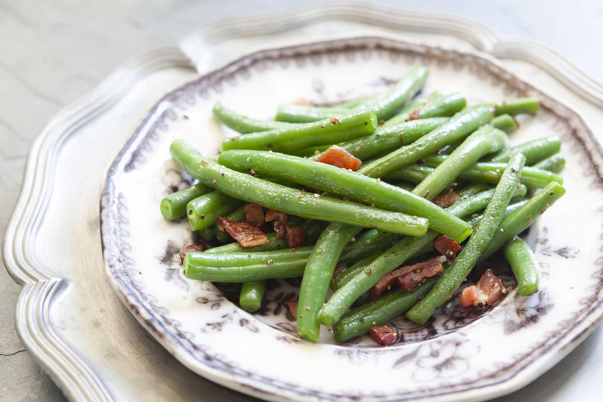 Side shot of fresh green beans, blanched and sauteed with bacon on a plate