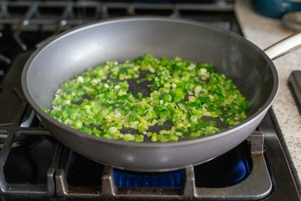 Green onions are sauteed in a non-stick skillet on a gas stove to make low carb cauliflower rice.