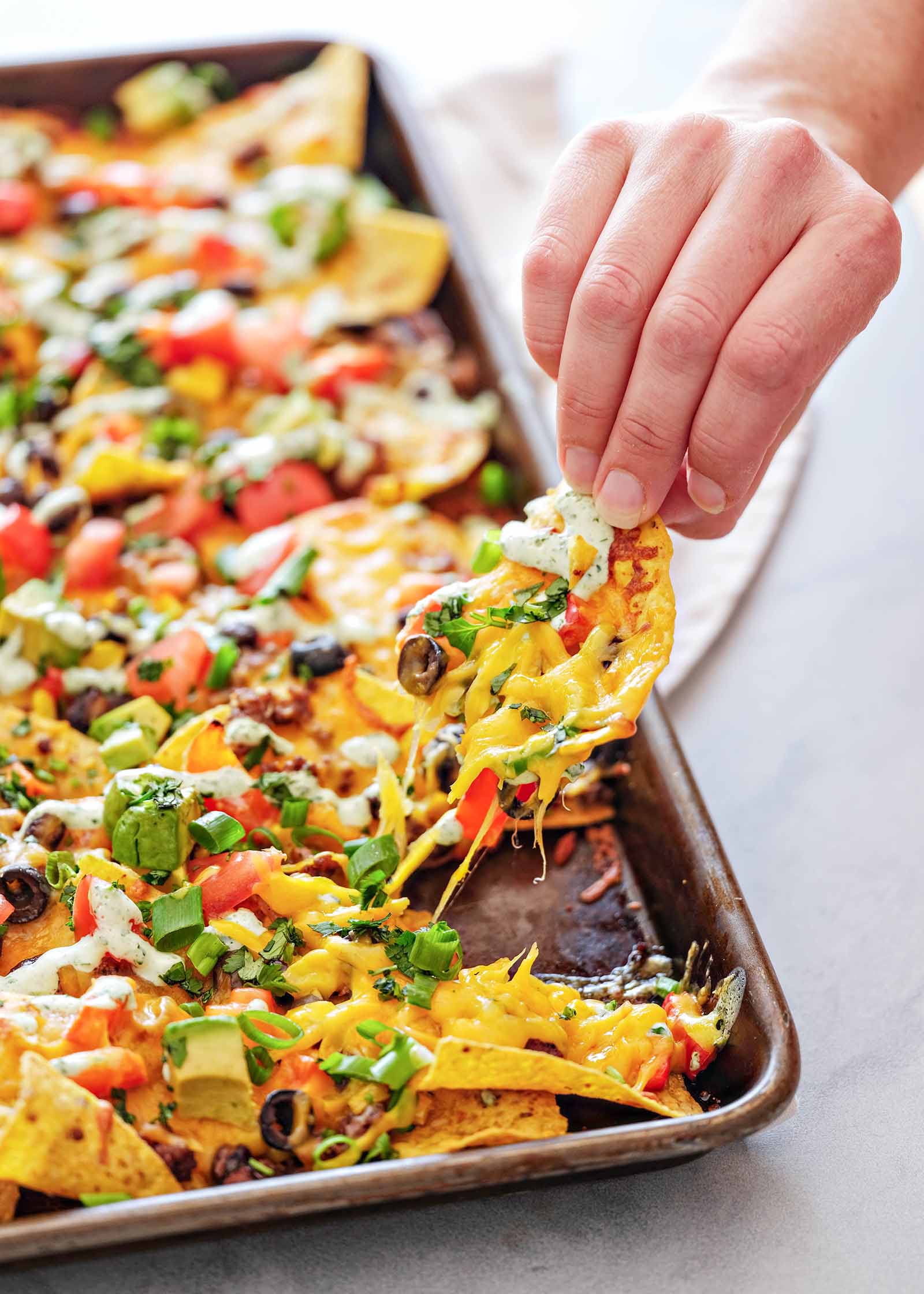 One loaded chip being removed from a batch of easy sheet pan nachos