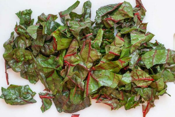 Chopped swiss chard leaves on a white cutting board. Stems are removed.