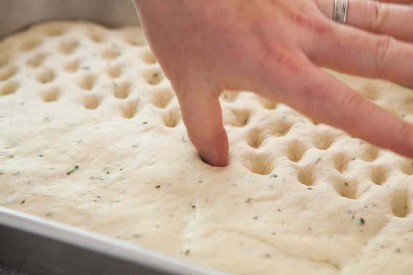 Dimple the top of the focaccia dough in the pan with your thumb