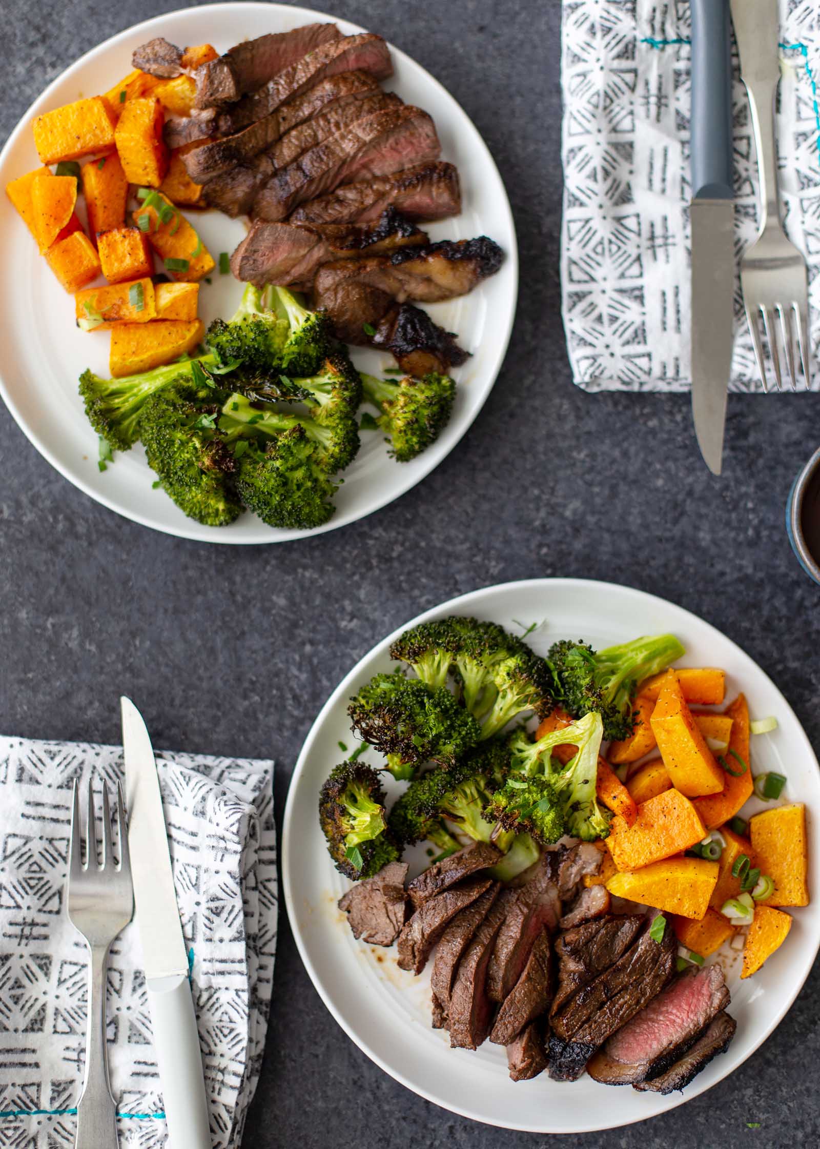 Two plates with sliced easy broiled steak, chopped broccoli and squash. Silverware and a linen are next to each plate.