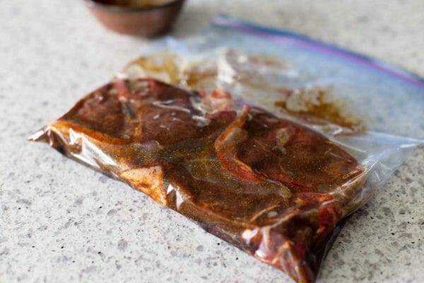 Steaks in marinade in a ziplock bag and on a kitchen counter.