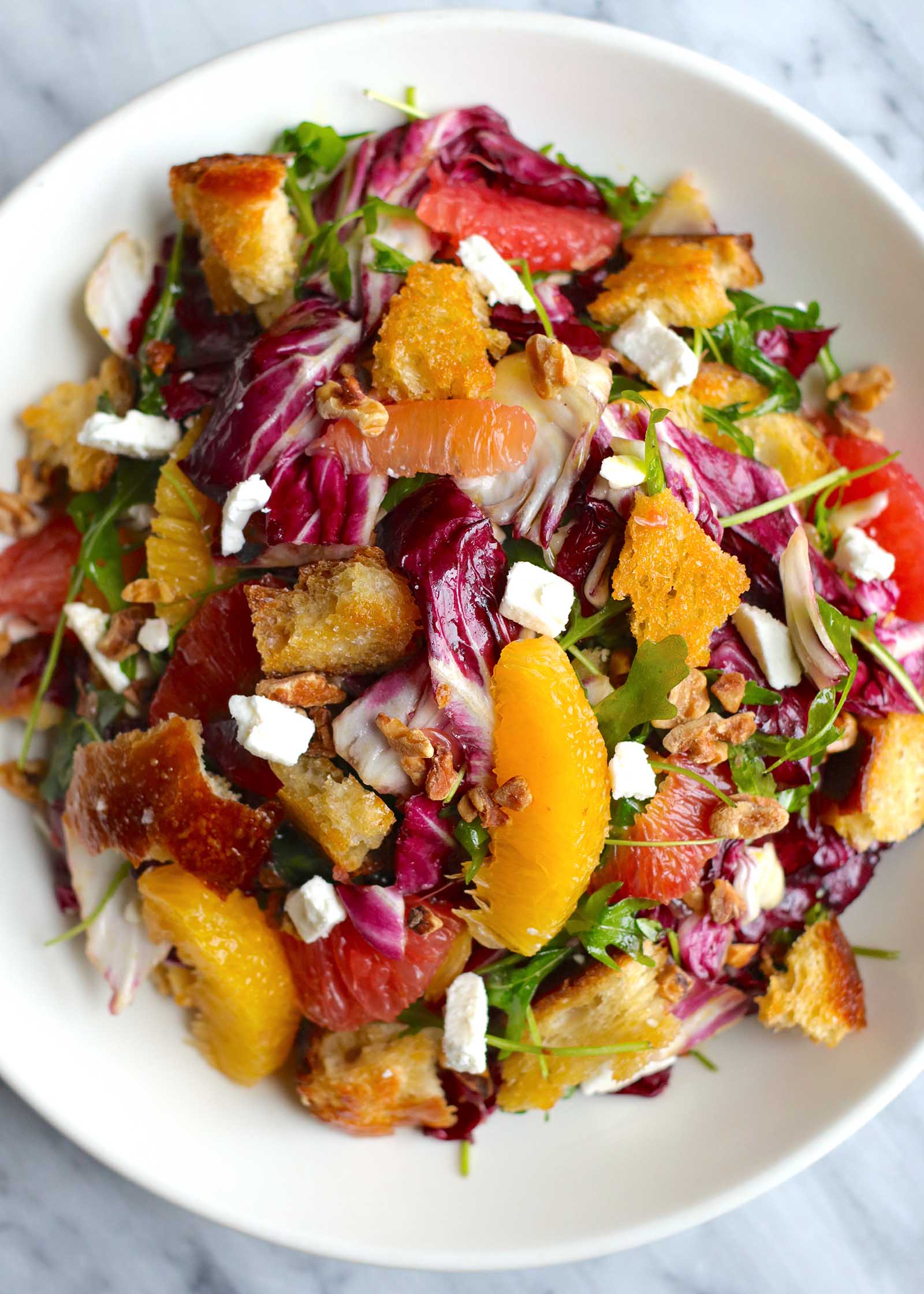 Citrus Salad on a white plate. Supremed orange and grapefruit, radicchio, croutons and feta cheese crumbles are visible.