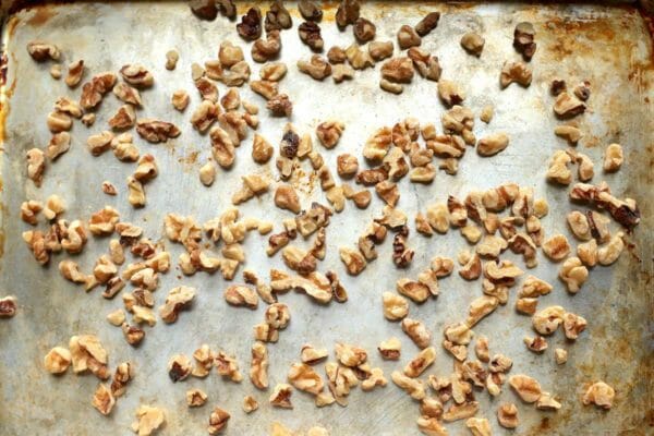 Overhead view of chopped walnuts on a worn baking sheet for a winter salad.