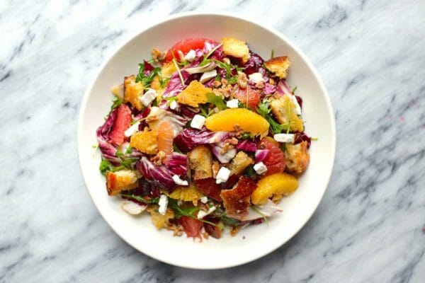 Citrus Salad on a white plate set on a marble background. Supremed orange and grapefruit, radicchio, croutons and feta cheese crumbles are visible.