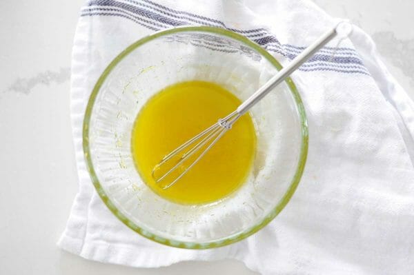 White dish towel wiht a small glass bowl of citrus honey dressing inside. A small whisk is inside the bowl.