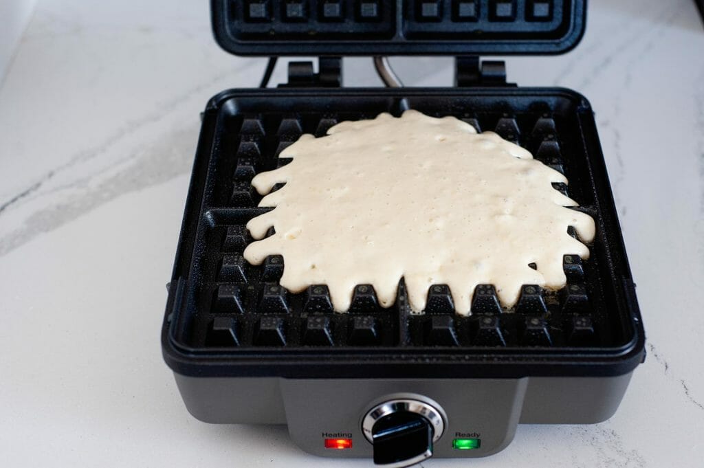 An open waffle maker with waffle batter in the center.