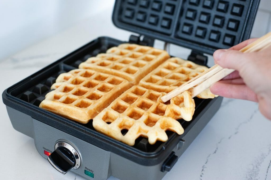 Chopsticks pulling a cooked waffle out of an open waffle maker.