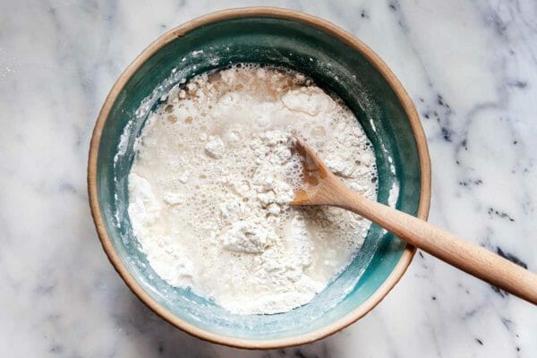 A wooden spoon stirs the ingredients for crusty homemade bread.