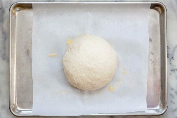 Easy No Knead Bread dough on a parchment covered baking sheet with cornmeal underneath it.