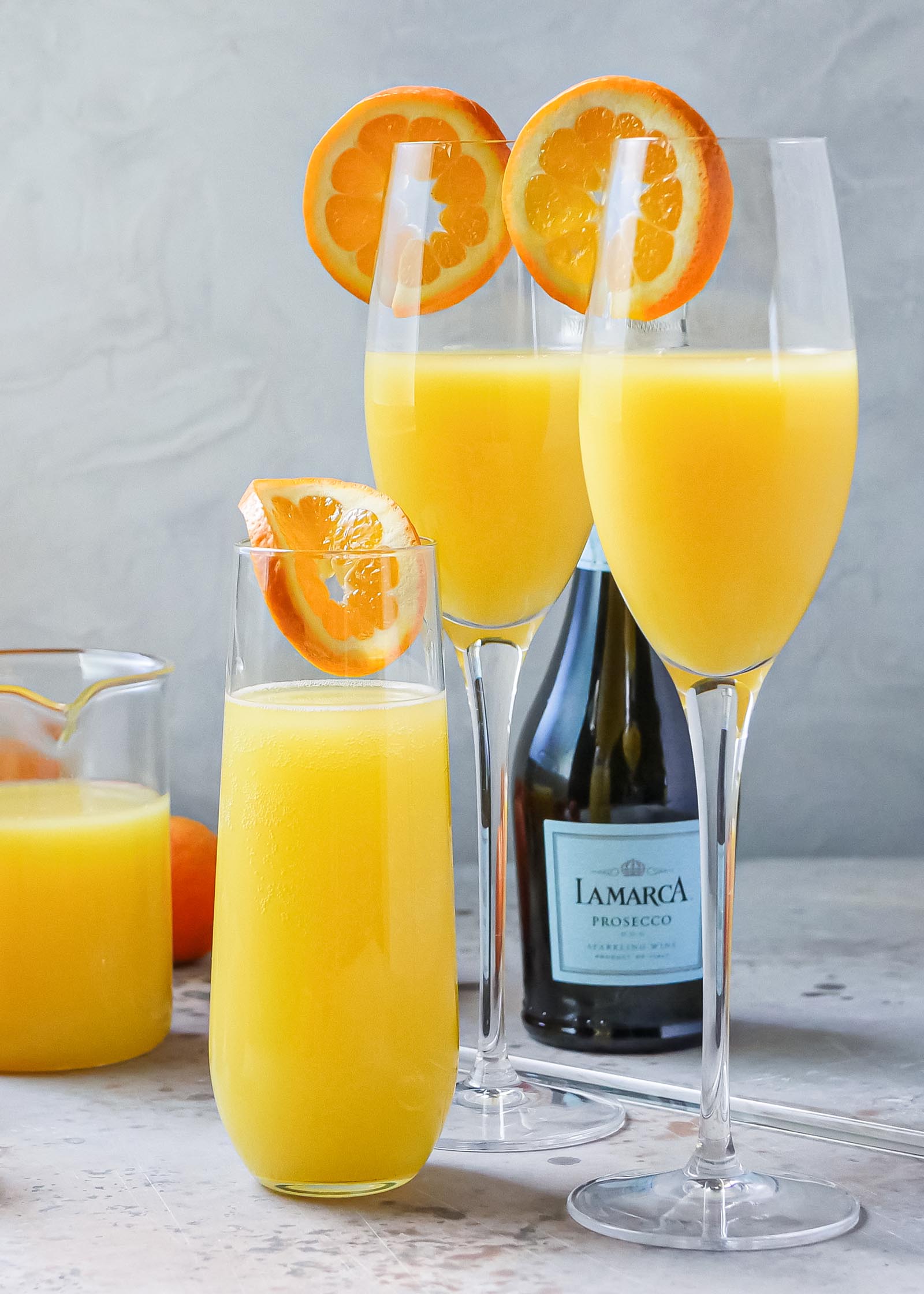 Classic mimosas in champagne flutes. Orange juice and prosecca are behind the glasses.