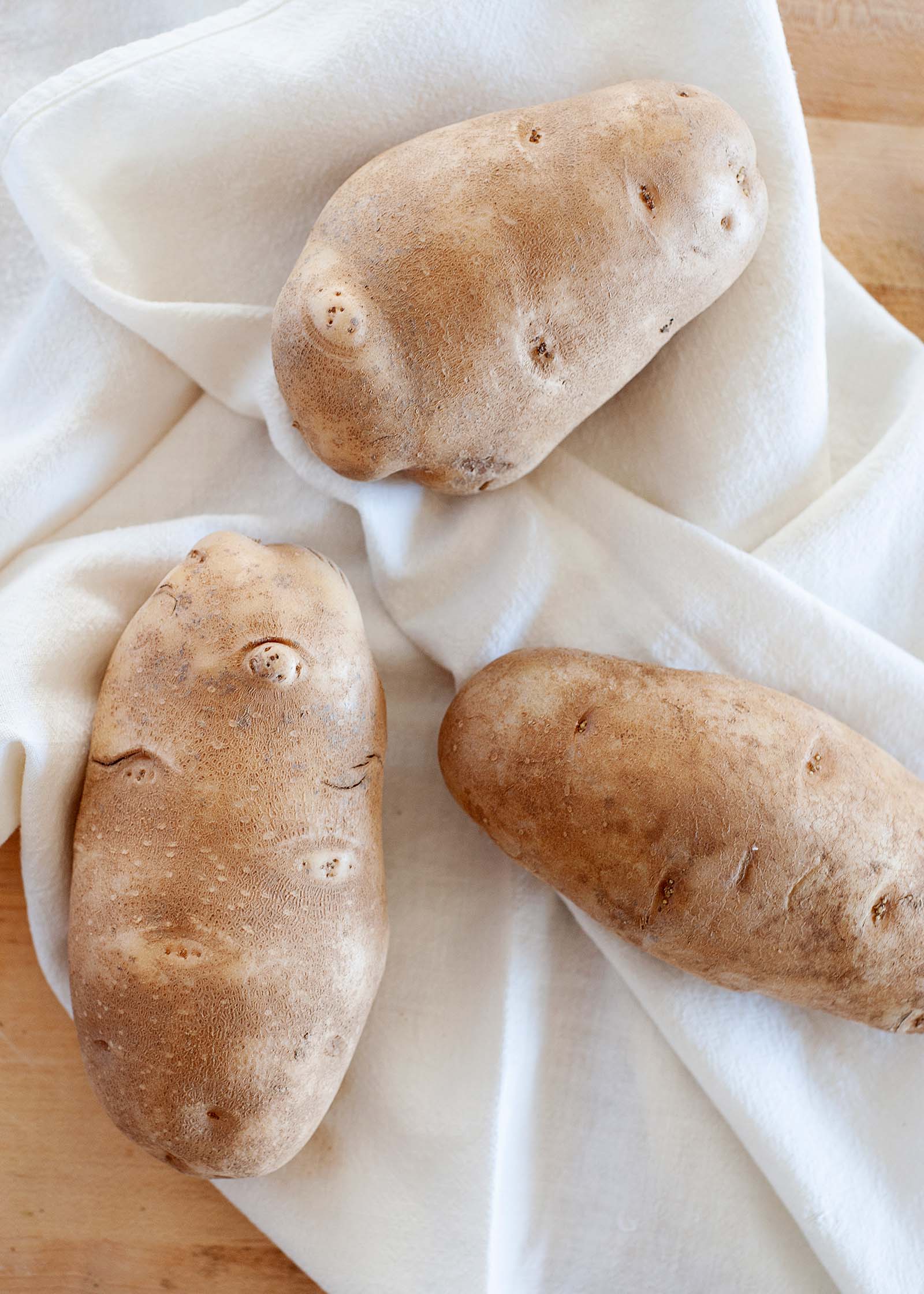 Three russett potatoes on a white linen.