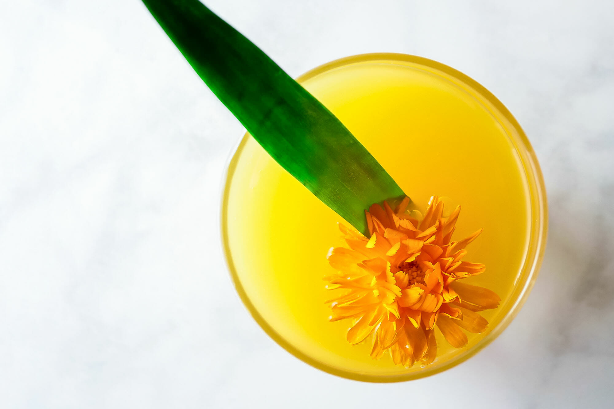 Overhead view of the bright orange Pineapple-Mango Mimosa. A flower and a pineapple leaf are inside the glass.