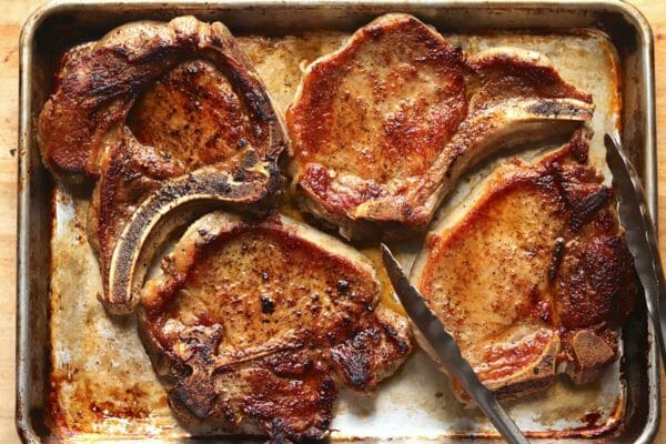 Four bone-in pork chops on a baking sheet to show how to cook pork chops.