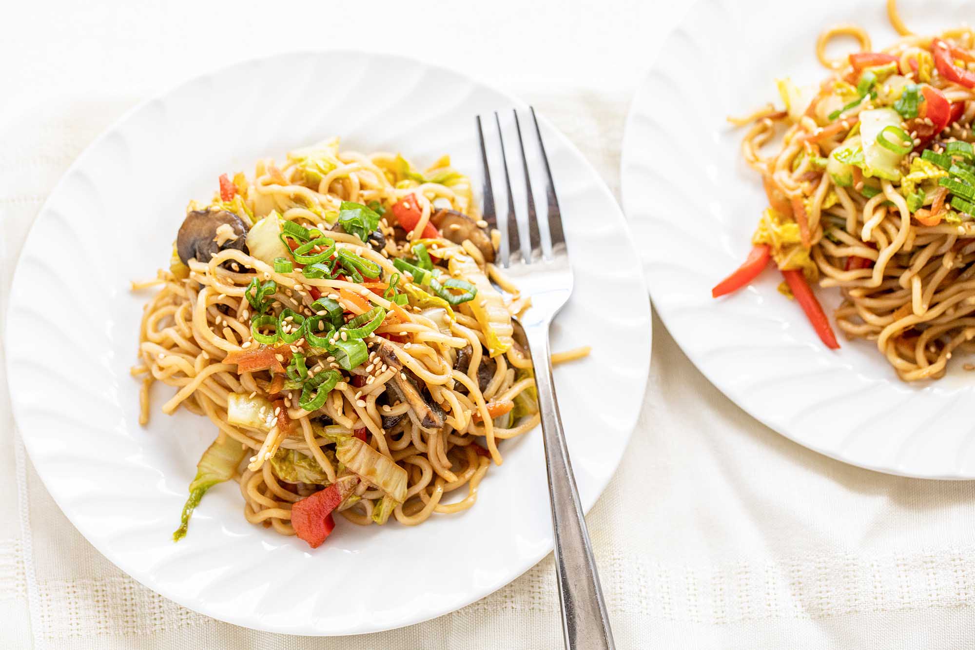 Two white plates and a fork with easy vegetable lo mein piled in the center of each.