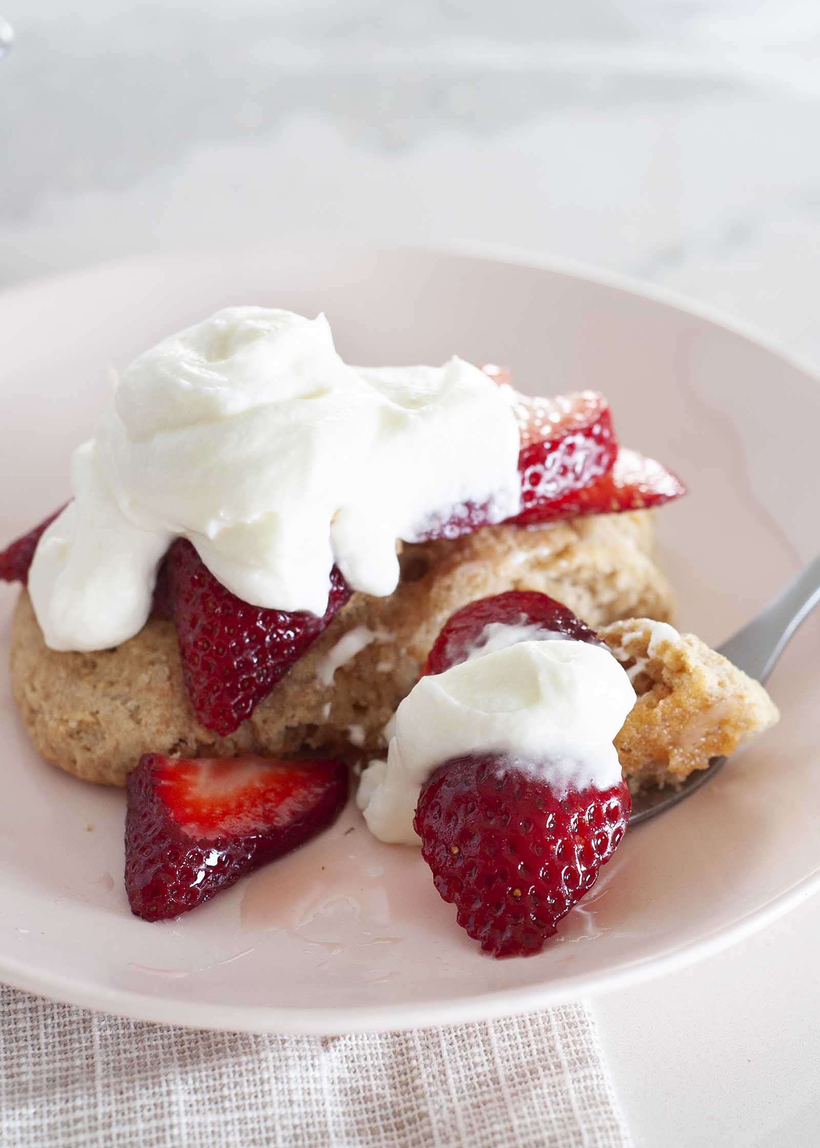 Close up view of healthy strawberry shortcake on a plate. A fork has sliced strawberries, whipped yogurt topping and shortcake on it.