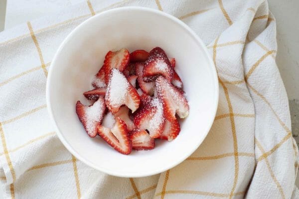 Sliced strawberries macerating in a small bowl to make easy strawberry shortcake.