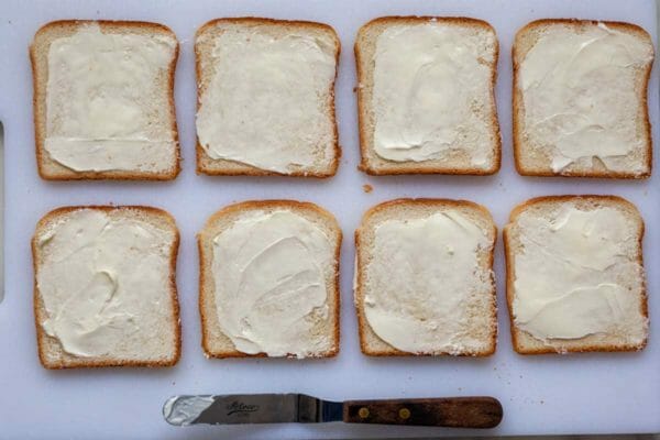 Eight slices of bread in two rows of four. Each slice is spread with butter to make cucumber sandwiches.