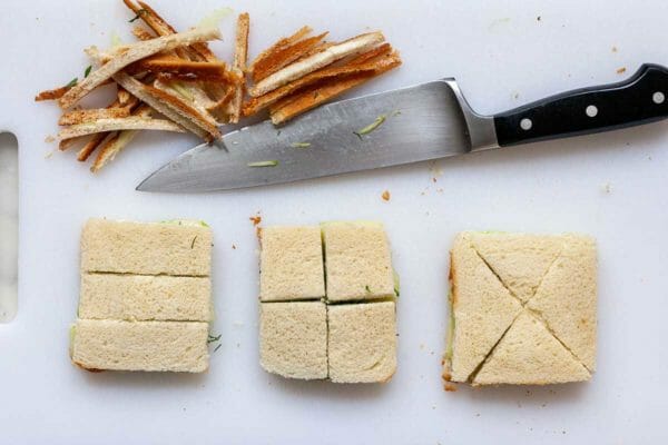 Showing different ways to slice cucumber tea sandwiches. A chef's knife is above three sandwiches and the crusts are cut off.