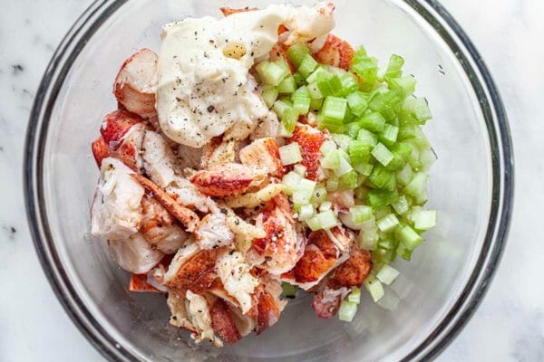 Glass mixing bowl with chopped lobster, mayo and diced celery to make a homemade lobster roll recipe.