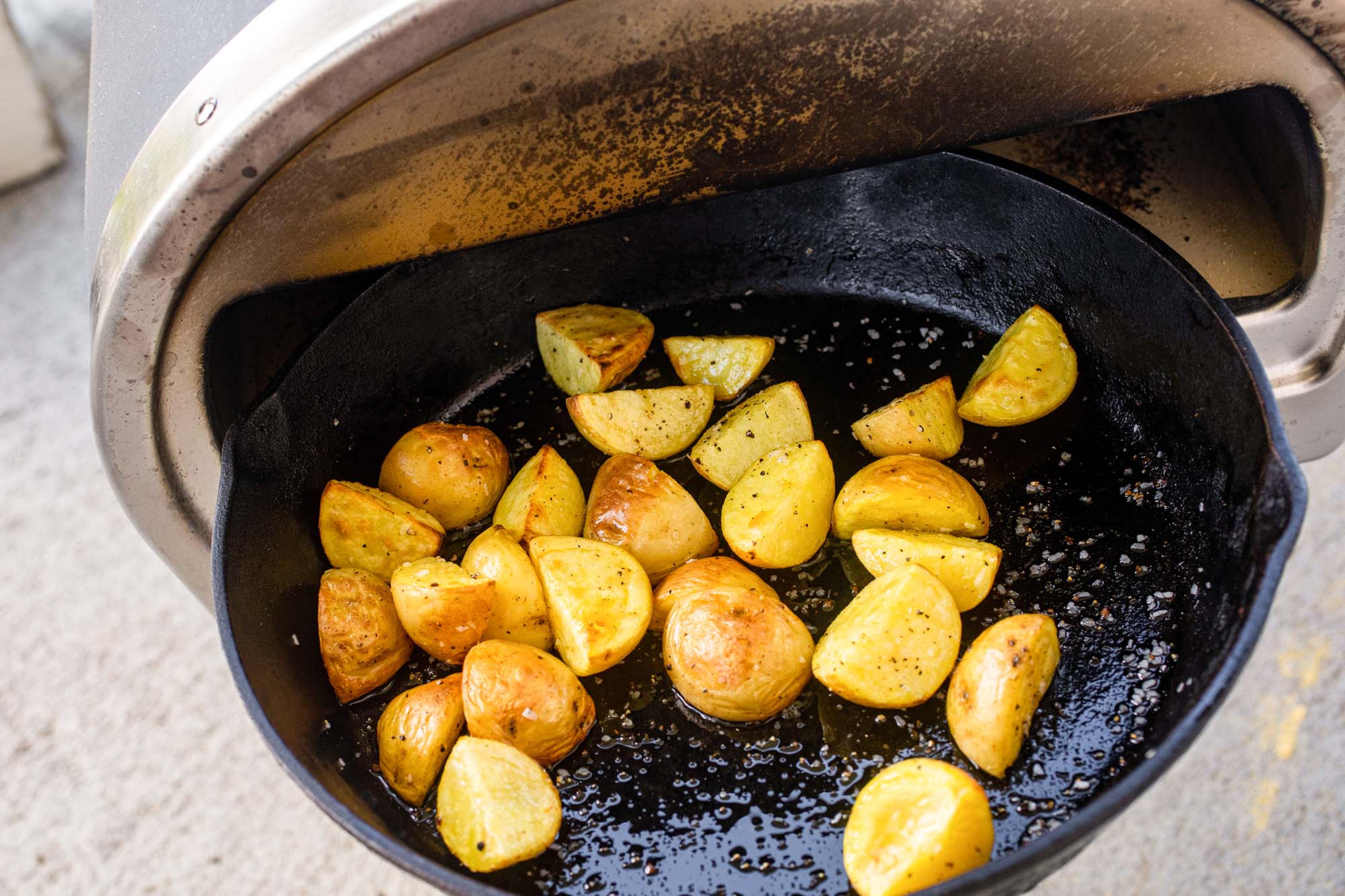 Cast iron skillet of quartered yukon gold potatoes cooked in a Roccbox.