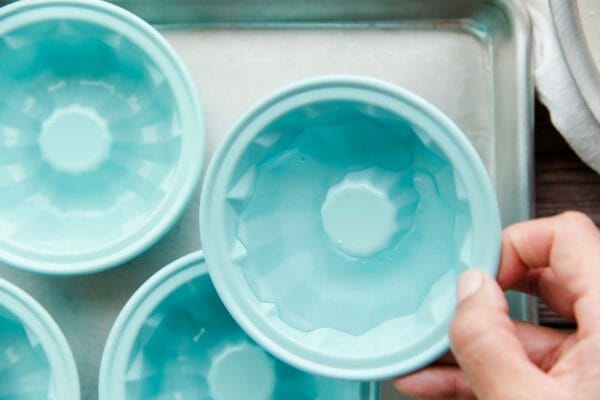Individual teal bundt pans are on a baking sheet. Cold water is at the bottom of the mold and being swished around.