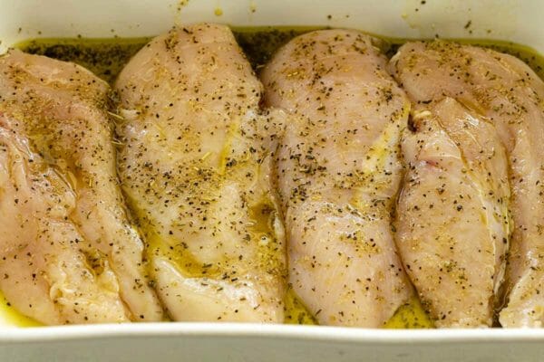 Four chicken breasts are marinating in a pan for chicken pasta skillet.