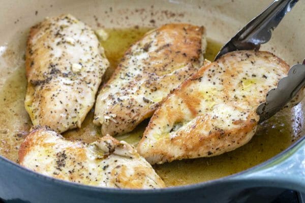Best tuscan chicken pasta is being made by cooking the chicken breasts in oil in a dutch oven.