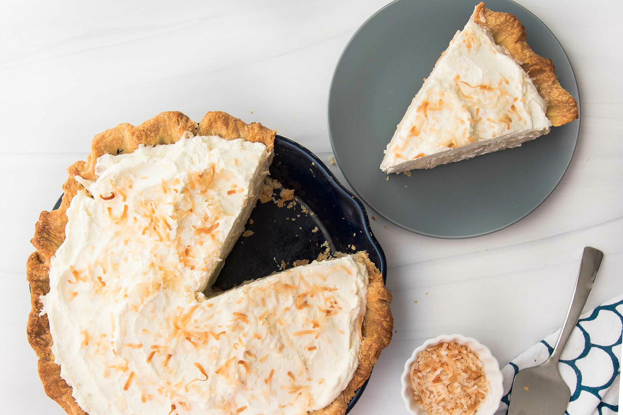 Overhead view of a homemade coconut cream pie with a slice removed and set on a plate to the right.