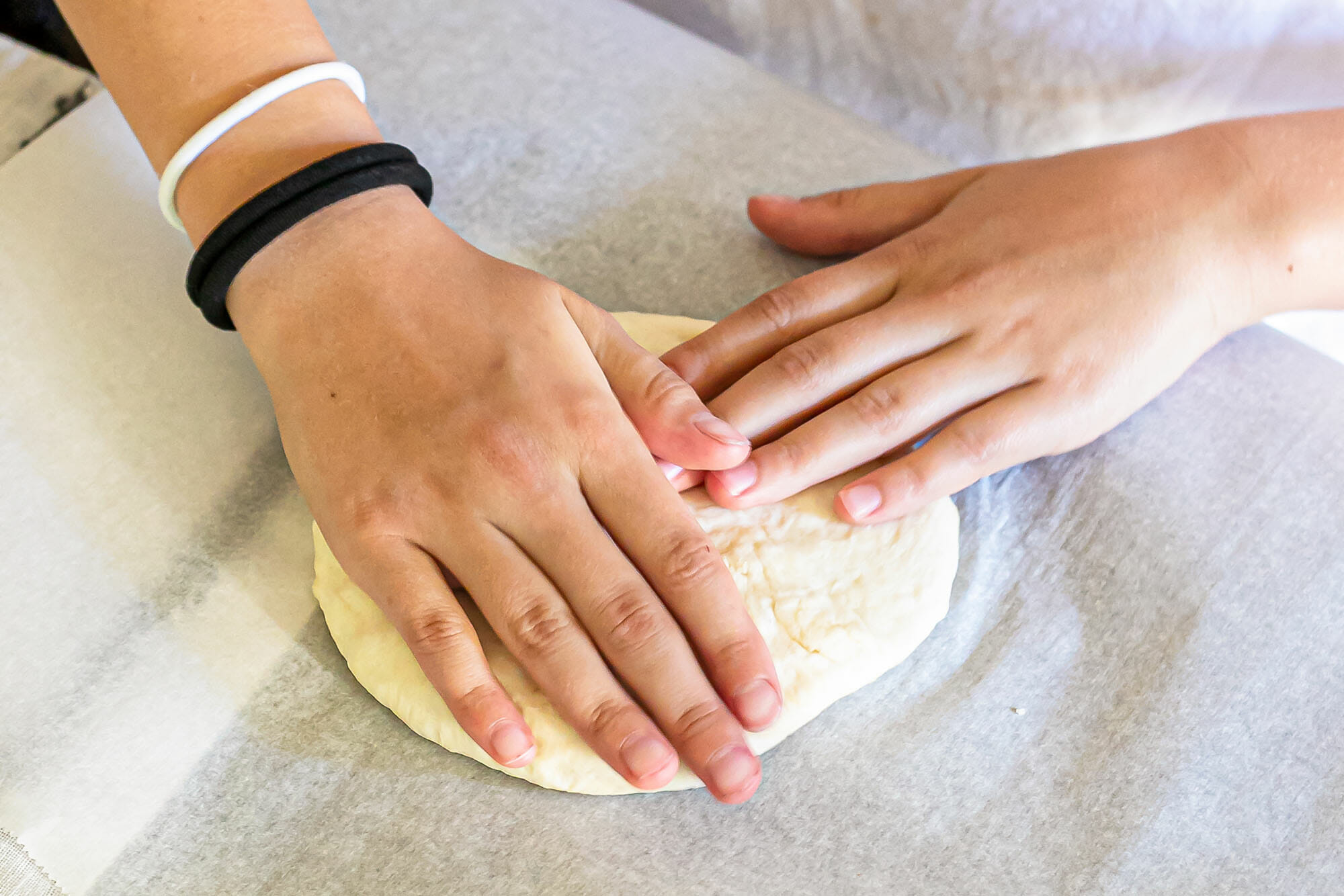 How to grill pizza. Hands flatten a pizza dough ball on a piece of parchment.