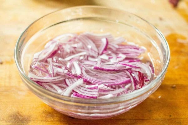 Sliced red onions soaking in vinegar in a prep bowl to make a vegetarian pasta salad.