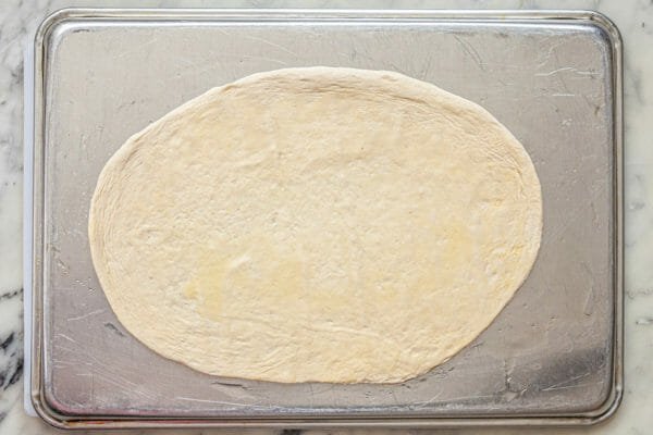 Pizza dough rolled out on the back of a baking sheet.