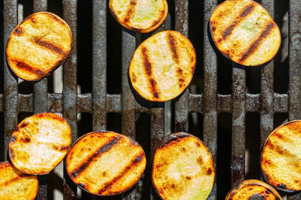 Zucchini coins on the grill with grill marks to make a grilled vegetable pizza.
