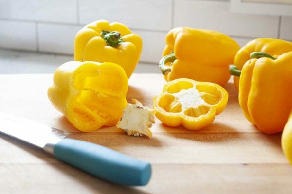 Side view of yellow bell peppers on a cutting board with a chef's knife to the left.