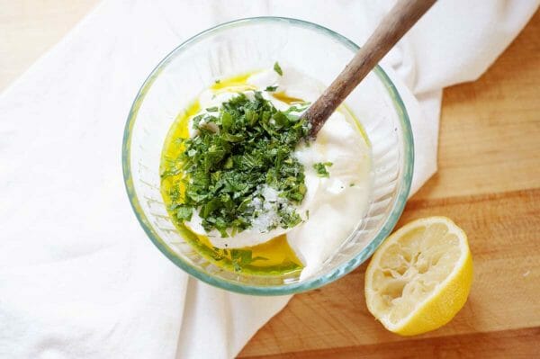 A glass bowl with yogurt, chopped mint, olive oil and lemon juice to make a yogurt mint sauce.