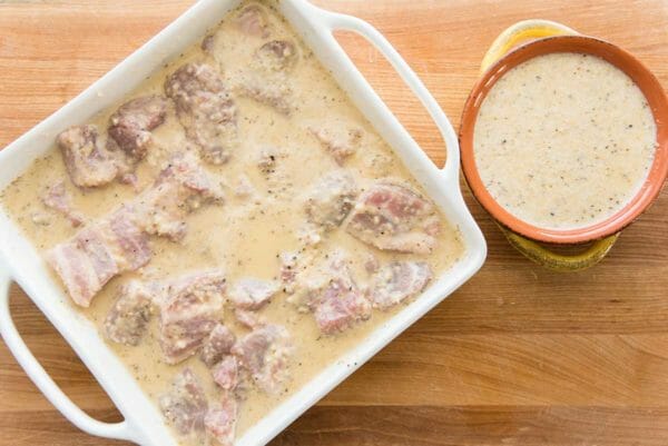 Bite sized pork are marinating in a casserole dish to make pork kebabs with mojo marinade.