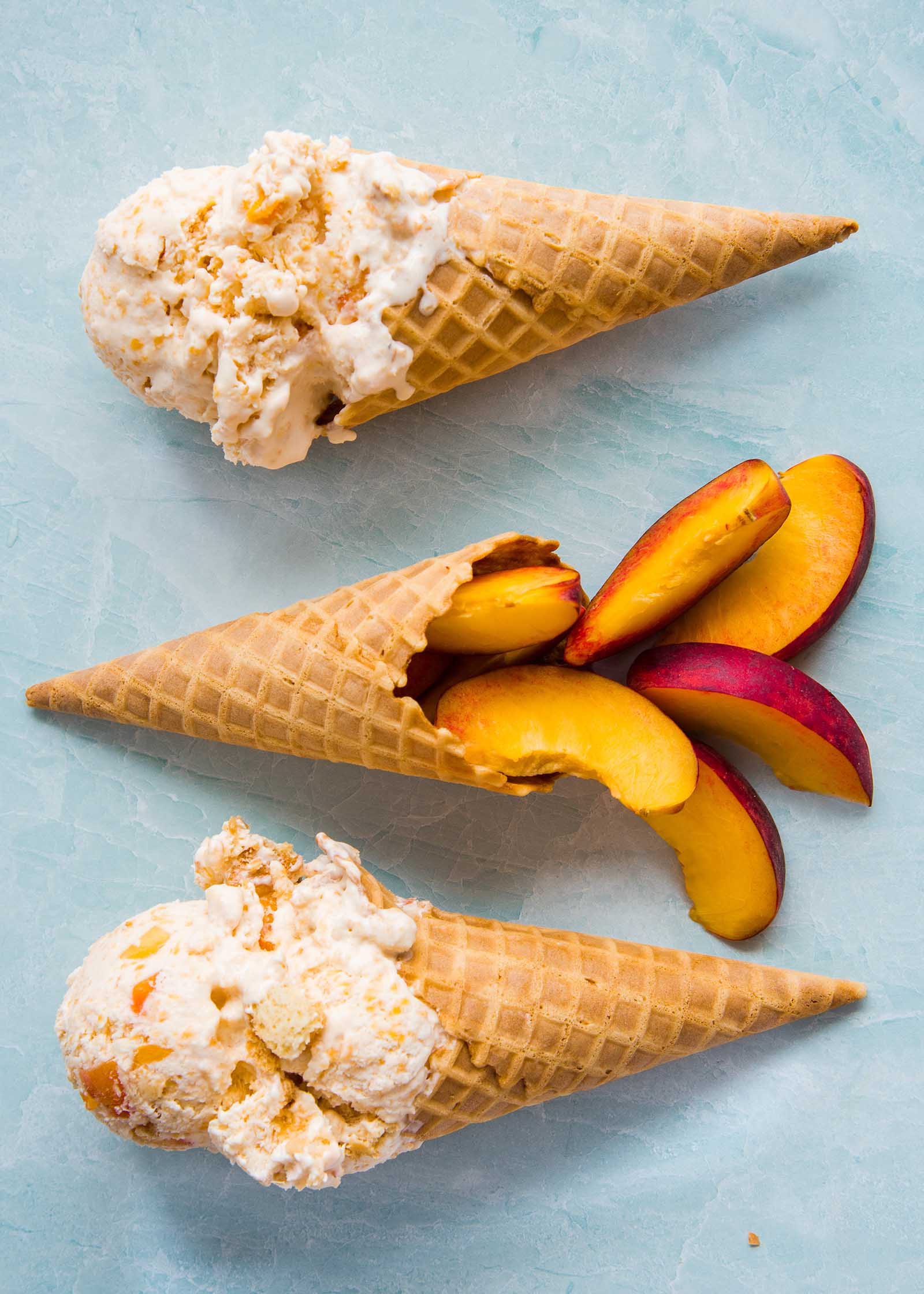 Two homemade peach cobbler ice cream cones are set on either side of a cone with sliced peaches.