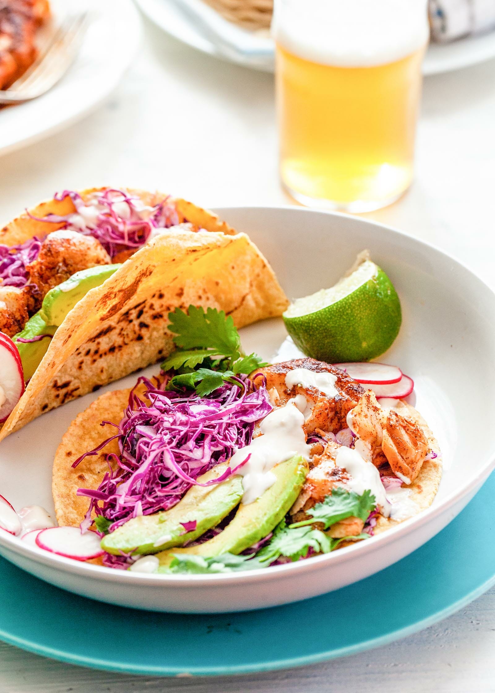 The best fish tacos on a plate. Corn tortillas layered with fish, cabbage, avocado, cilantro and lime.