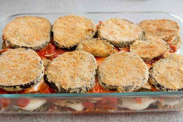 Baked eggplant layered in a casserole dish with mozzarella, tomato sauce and parmesan. The eggplant is crispy on top.